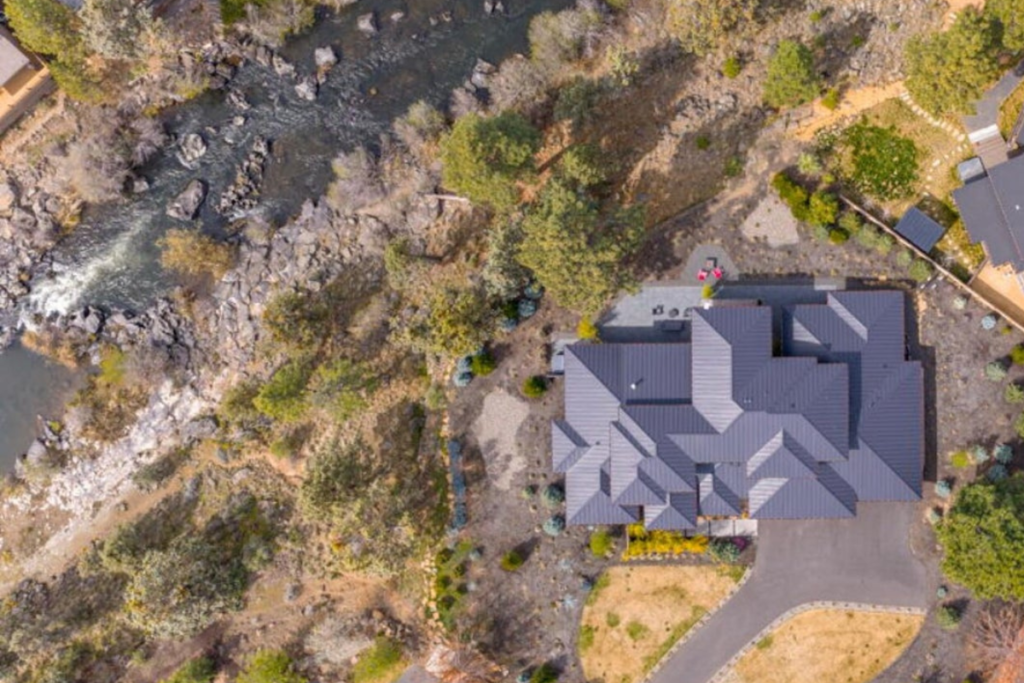 Aerial view of a Deschutes River home in Bend, Oregon, showing the residence beside the river and surrounding Central Oregon landscape