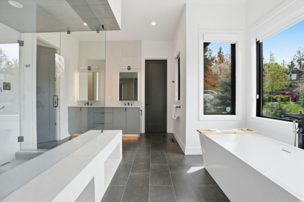 Modern primary bathroom with soaking tub, glass shower and large windows overlooking the landscape