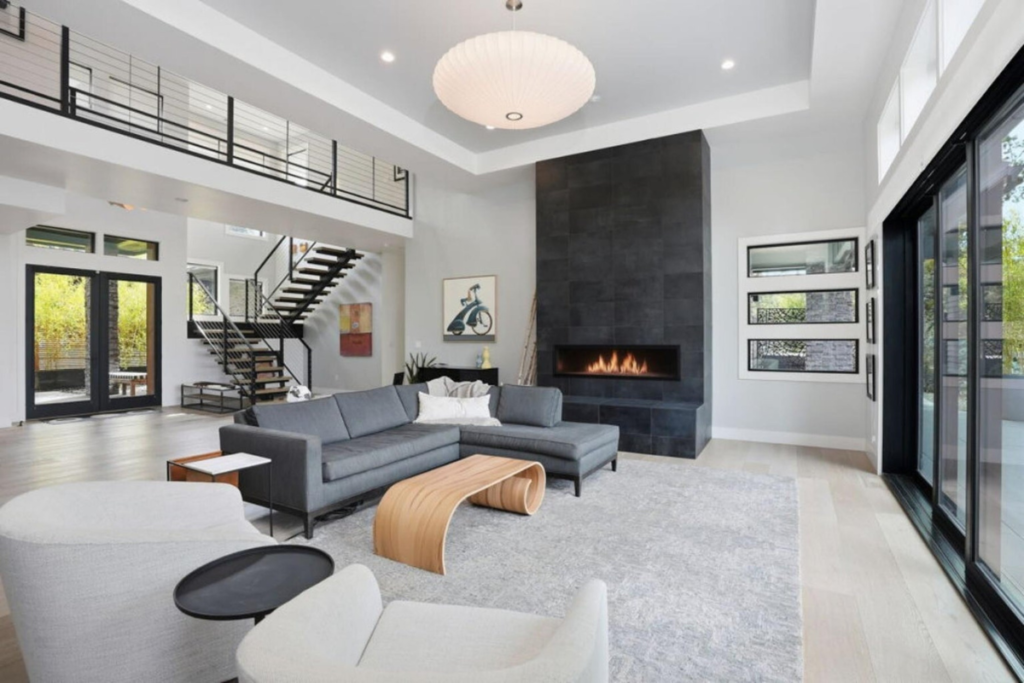 Modern living room with floor-to-ceiling windows, fireplace and open staircase in a Deschutes River home